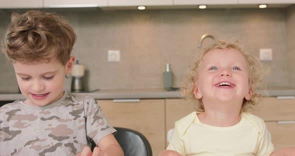 Adorable Brother and Sister Smile and Laugh Together While Sitting at the Kitchen Table Boy Holds alt