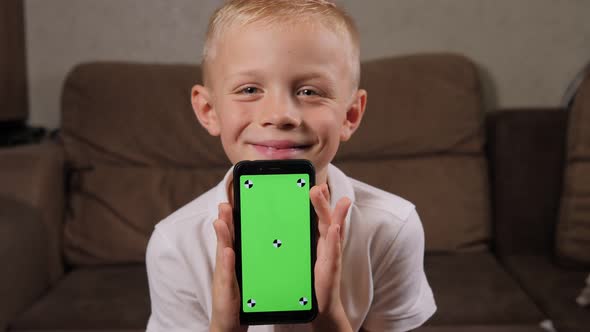 A Little Boy Sitting on the Couch and Holding a Phone with a Green Screen alt