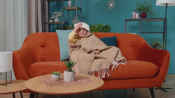 Child Girl in Plaid Suffering From Cold or Allergy Blows Nose Snot Into Napkin on Sofa at Home alt