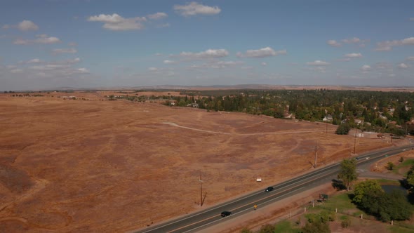 Aerial drone view flying over a dry empty field beside a highway in California. alt