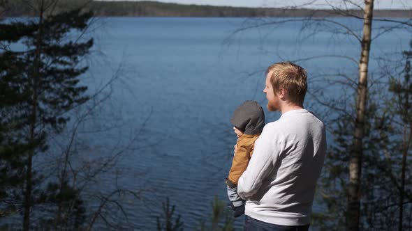 father with his son in his arms standing with his back looking at the lake