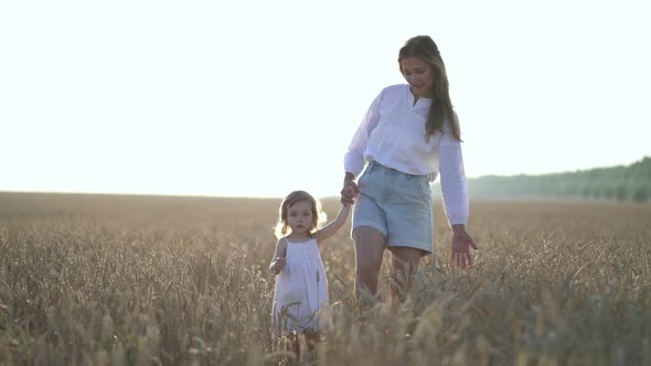 Little Daughter and Mom Walk Around Wheat Field Holding Hands