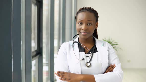 Young African Woman Doctor or Nurse Standing in Medical Suit at Clinic and Looking at Camera alt