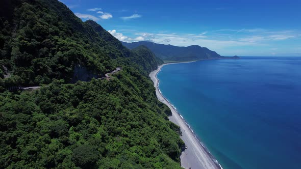 Flying Parallel to a narrow cliff-side highway with scenic views of lush greenery along the majestic alt