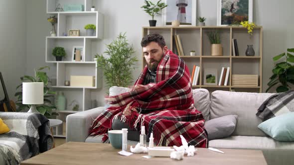 Ill Man with Chills and Wraps Himself in a Blanket on the Sofa in Living Room alt