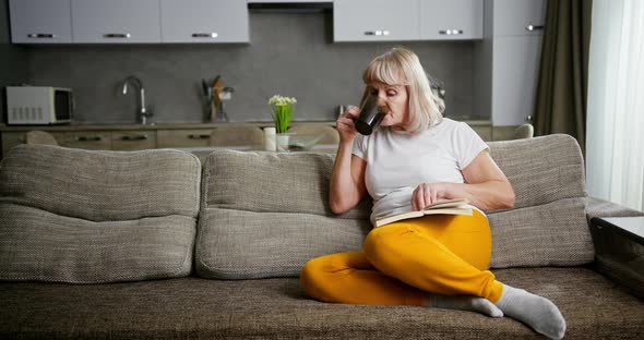 Senior Woman or Grandmother Relaxing on a Sofa Reading a Book and Enjoying a Mug of Hot Tea or alt