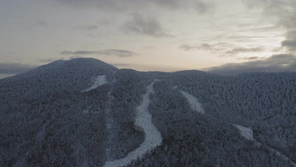 Abandonded ski lift and trails at the peak of a snow covered mountain AERIAL PULL BACK alt