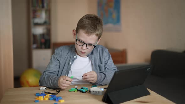 Caucasian Boy with Glasses Creates His Own Model of Robot From Constructor alt