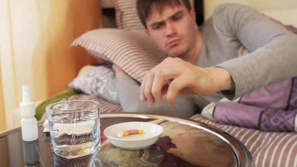 Sick Man Taking Pill While Lying On Bed.  alt