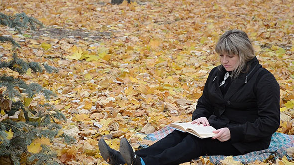 A Woman Reading a Book in Autumn Park