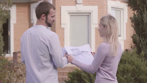 Back View of Two Caucasian People Standing in Front of the House with Architectural Drawings alt