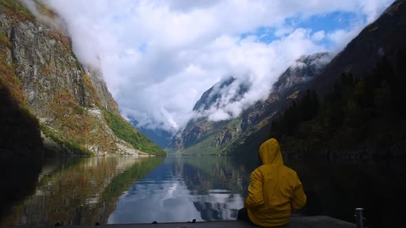 Beautiful fjord landscape at Sognefjord of Norway. Man in yellow raincoat sitting at the edge of a q alt