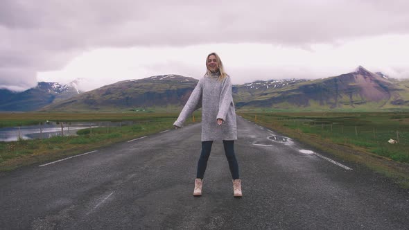Happy Young Woman Dancing on Asphalt Road in Iceland and Having Some Fun Slow Motion alt