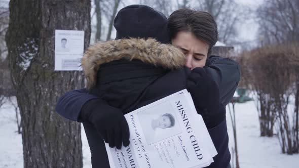 Back View of Man in Winter Clothes Hugging Desperate Young Caucasian Woman. Mother Holding Ads with alt
