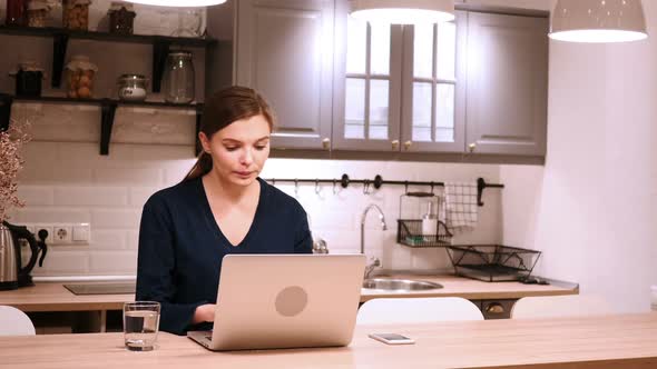Woman Celebrating Online Success While Working on Laptop in Kitchen alt