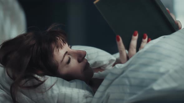 Pretty Brunette Woman Covered with a Blanket Lies on the Bed and Reads a Book at Night Cinematic alt