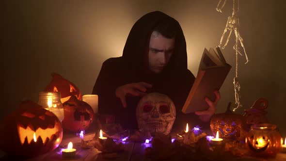 A Spooky Wizard is Reading a Magic Book and Conjuring Over the Skull on the Black Background alt