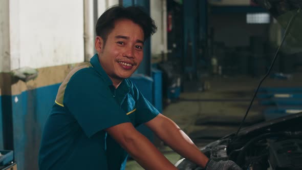 Professional car mechanic looking at camera and smiling at repair service station.