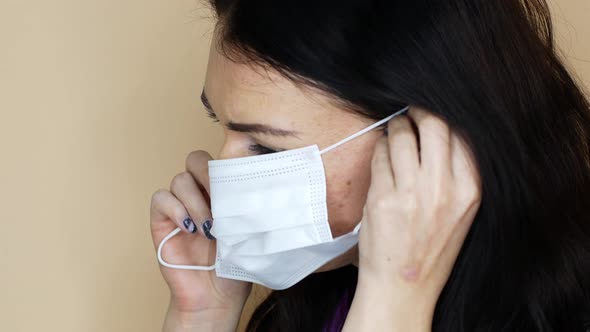A woman in a medical uniform puts on a white sterile mask before the procedure. alt