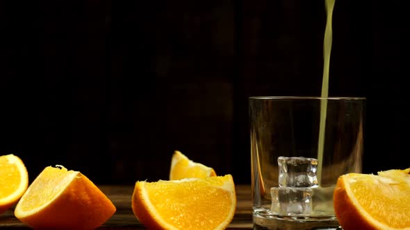 Juice Is Poured Into A Glass With Ice, Several Sliced Oranges On The Table