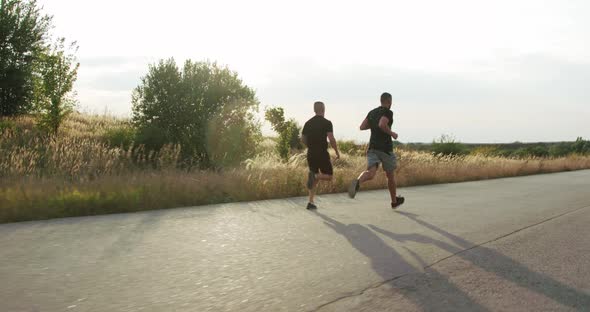 Two Sportsmen Jogging on a Path Synchronously at Nature on Sunset alt