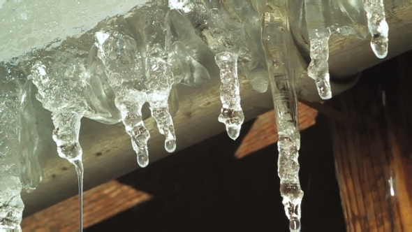 Melting Icicles Dripping From Roof Eaves In Spring