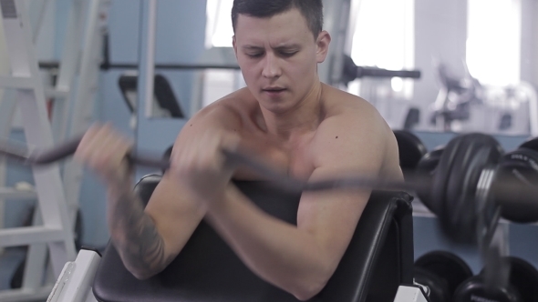 Man Shakes His Biceps Sitting On The Simulator