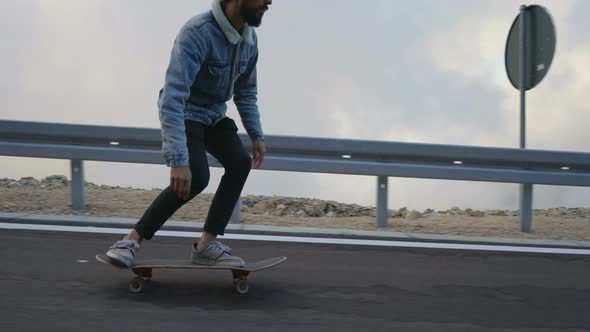 Young Man with a Beard Riding Skateboard Cruising Downhill on Countryside Road