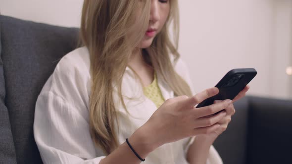 Asian woman in white shirt sitting on the sofa and using smartphone.