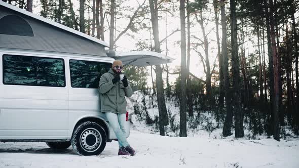 Man Drinks Standing in the Back of a Van with Pop Up Roof in the Woods in Winter