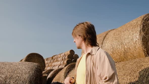 Farmer Agronomist Checks Hay Bales on the Wheat Field After Harvest at Sunset alt