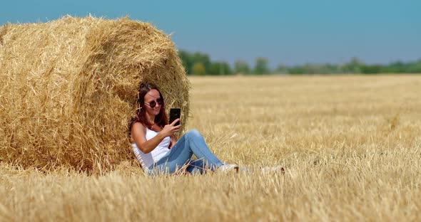Happy Girl is Sitting By a Large Haystack and Taking a Photo on a Mobile Phone a Photo Shoot in a alt