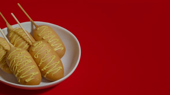 Moving Shot of Red Background with White Plate and Five Corn Dogs with Sauce alt