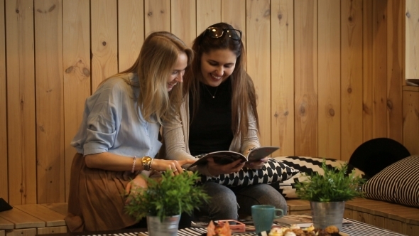 Two Girls Reading Magazine And Smilling In Cafe