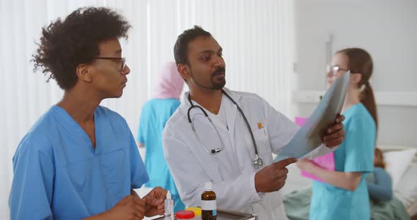 Indian Doctor and African Intern Studying Xray of Patient in Hospital Ward alt