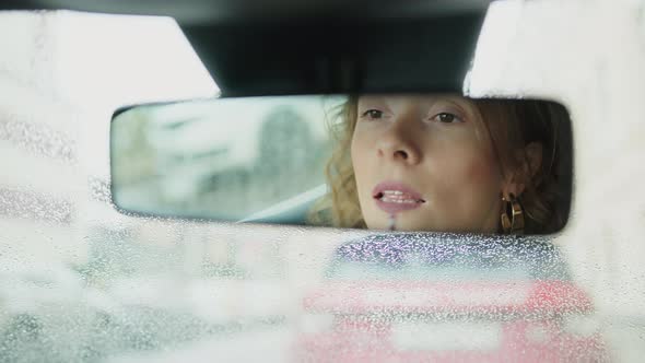Closeup of Woman Painting Her Lips in the Reflection of the Car Rearview Mirror alt