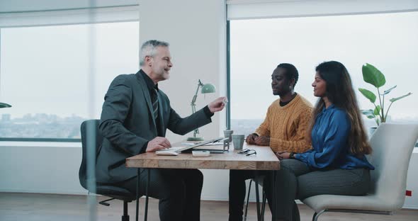 Real estate agent discussing house rental contract with couple and handing them keys alt