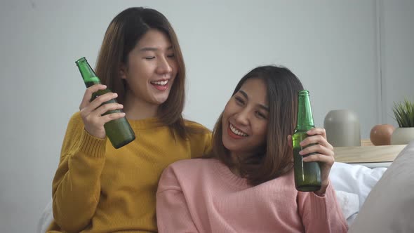 Asian lesbian lgbt couple sitting at sofa and drinking beer in living room. alt