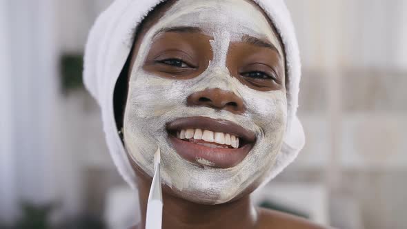 African American Girl in white Towel on Head Applying Mask on Face alt