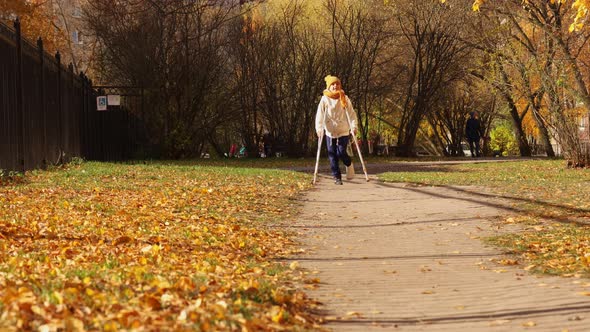 Kid Walks in Autumn Park on Crutches