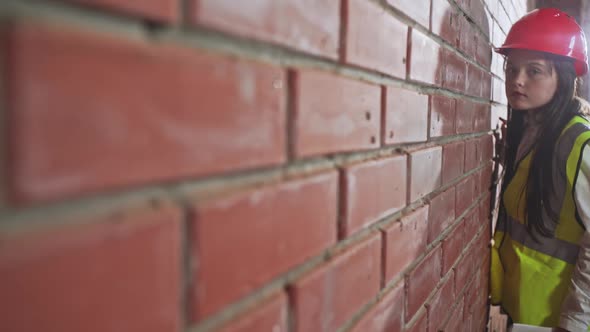 Girl in the Protective Building Helmet and Vest Checks the Quality of Work on the Construction of a alt