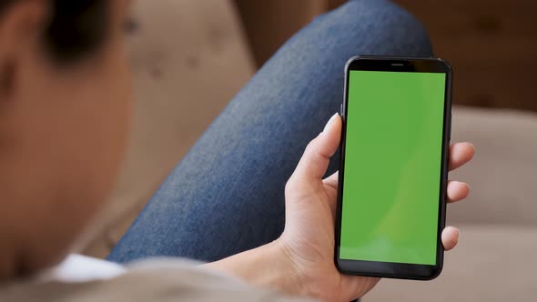 Young woman sitting on a couch and using smartphone with green screen alt