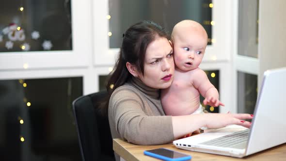 Young Woman with Toddler in Arms Typing on Laptop Remote Work with a Baby at Home