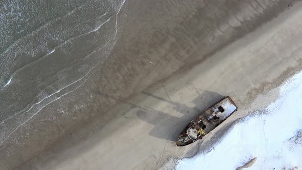 Aerial Top View of Old Wrecked Fishing Ships Drowned at the Sea Shore in Snowy Winter Season alt