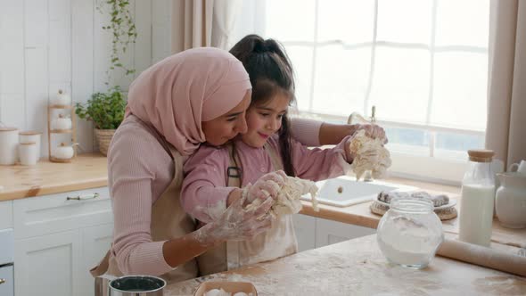 MiddleEastern Mom And Daughter Kneading Dough Together Baking In Kitchen alt