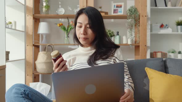 asian woman hold medicine sit on couch video call with laptop consult with doctor at home.