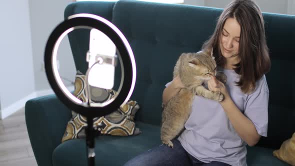 Woman Blogger with Her Cat Is Shooting a Video on Smartphone Using Ring Lamp alt