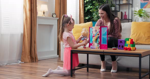 A Cheerful Mom is Playing with Pretty Daughter Dressed in a Pink Dress alt