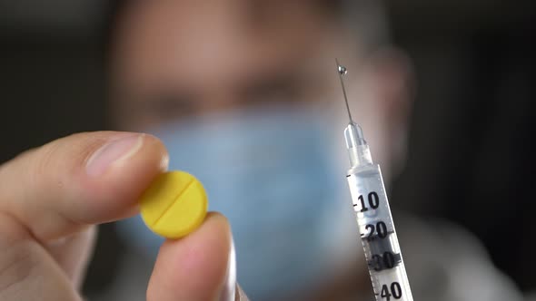Doctor in Medical Face Mask Offering Pill or Syringe alt