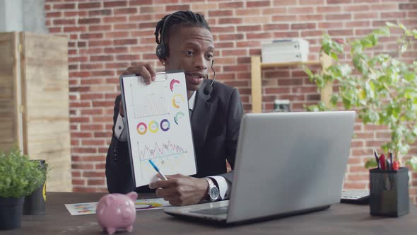 Black man businessman sitting at an office table holds a sheet with diagrams alt
